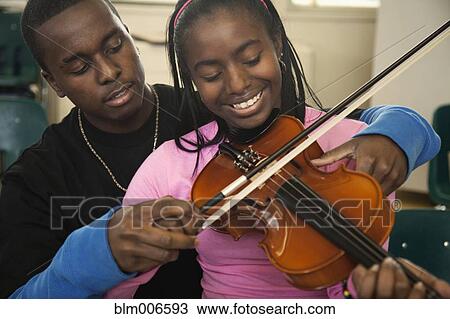 Stock Image - Teenager helping friend learn to play violin. Fotosearch