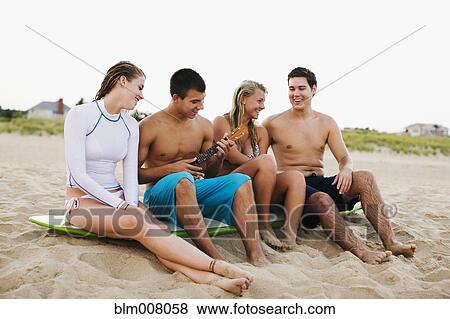 Stock Photo - Teenagers sitting on surfboard and playing ukulele on beach. Fotosearch