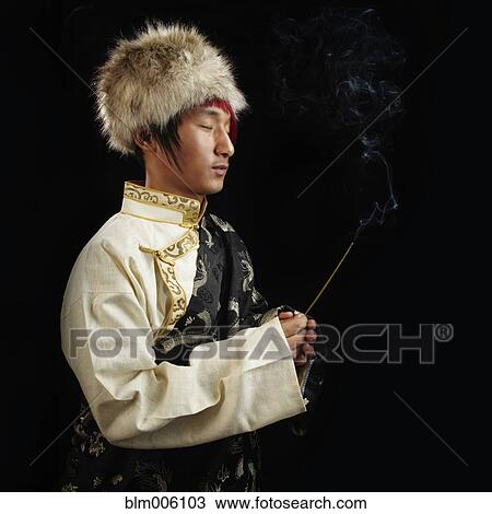 Stock Image - Tibetan man in traditional clothing with incense. Fotosearch