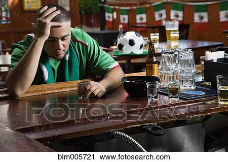 Stock Image - Unhappy man drinking in sports bar. Fotosearch