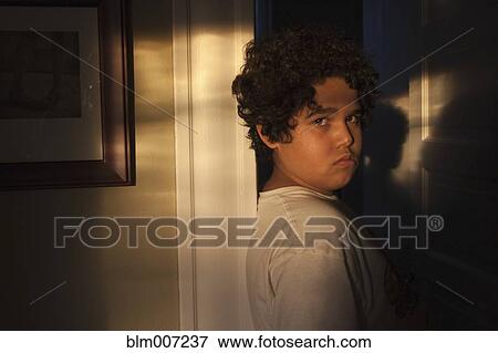 Stock Photo - Unhappy mixed race boy in doorway with shadows. Fotosearch