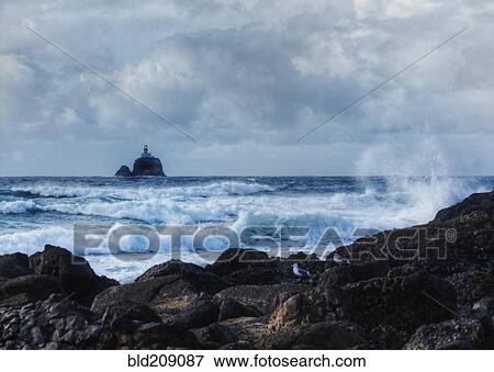 Stock Photo - Waves crashing on rocky beach with lighthouse in distance, Tillamook, Oregon, United States. Fotosearch
