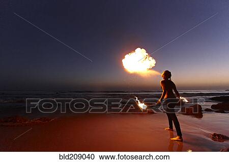 Stock Image - Woman breathing fire on beach. Fotosearch