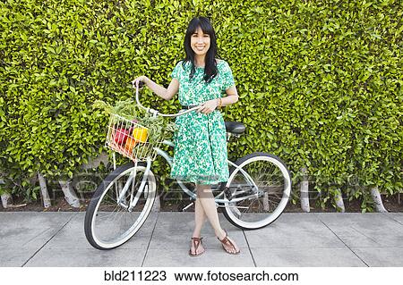 Stock Image - Woman carrying produce in bicycle basket. Fotosearch