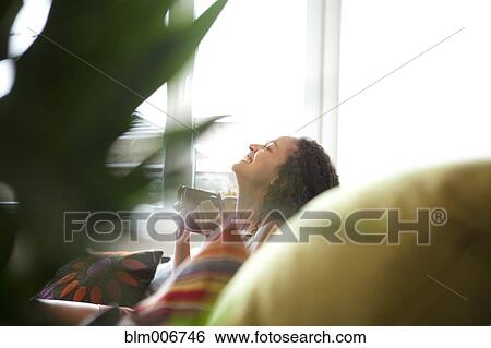 Stock Photograph - Woman drinking coffee in living room. Fotosearch