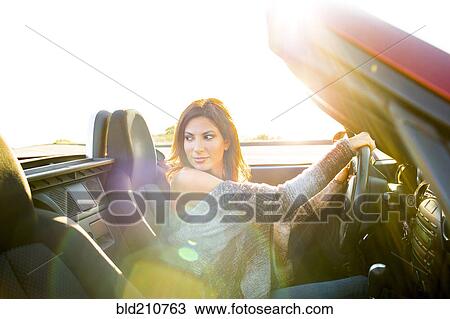 Stock Image - Woman driving convertible at sunset. Fotosearch