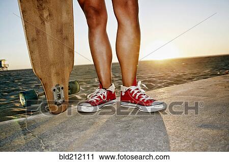 Stock Image - Woman holding longboards on beach. Fotosearch