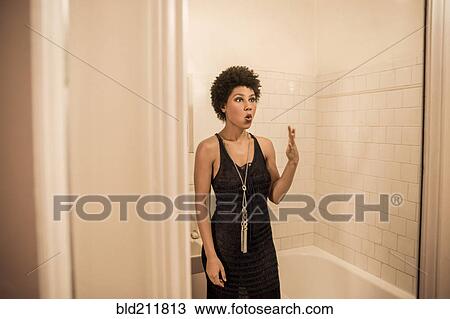 Stock Image - Woman making a face in bathroom mirror. Fotosearch