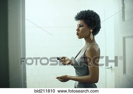 Stock Image - Woman putting on makeup in bathroom. Fotosearch