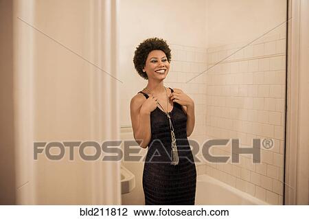 Stock Image - Woman putting on necklace in bathroom. Fotosearch