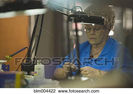 Stock Image - Woman repairing circuit board. Fotosearch