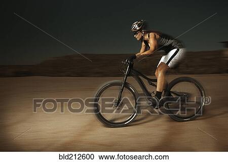 Stock Image - Woman riding mountain bike in desert. Fotosearch