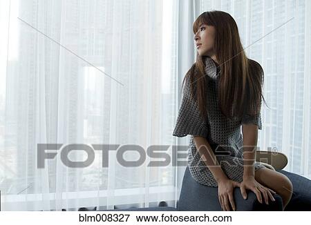 Stock Photo - Woman sitting on chair near curtain. Fotosearch