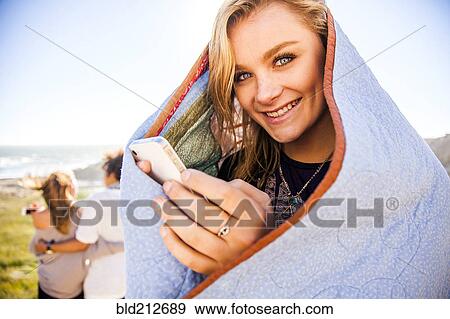 Stock Photo - Woman using cell phone in blanket on rural hillside. Fotosearch