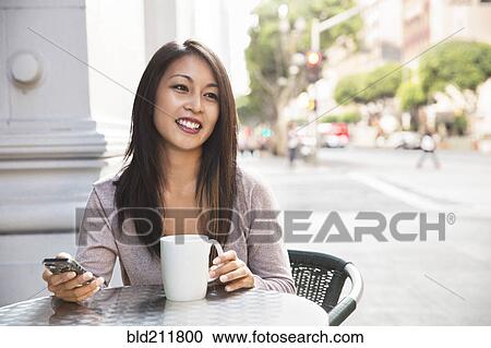 Stock Image - Woman with cell phone enjoying coffee at sidewalk cafe. Fotosearch