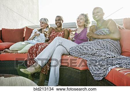 Picture - Women drinking wine together on urban rooftop. Fotosearch