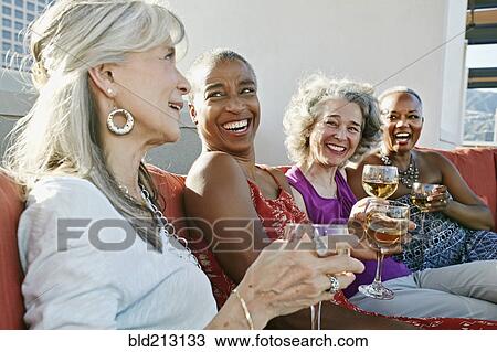 Stock Image - Women drinking wine together on urban rooftop. Fotosearch
