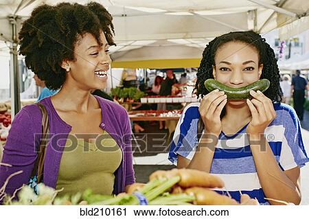 Stock Image - Women smiling together at outdoor market. Fotosearch