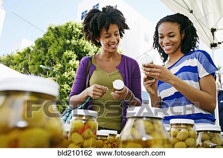 Stock Image - Women smiling together at outdoor market. Fotosearch