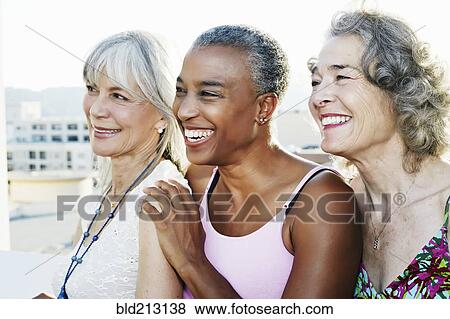 Stock Photo - Women smiling together on urban rooftop. Fotosearch
