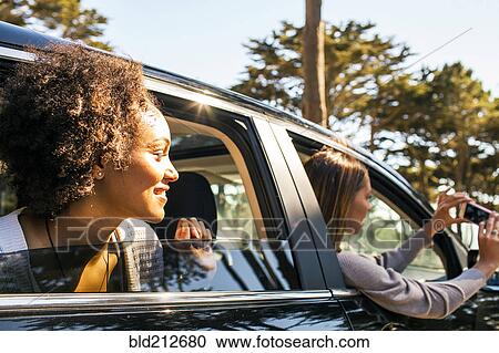 Stock Image - Women taking cell phone picture together in car. Fotosearch