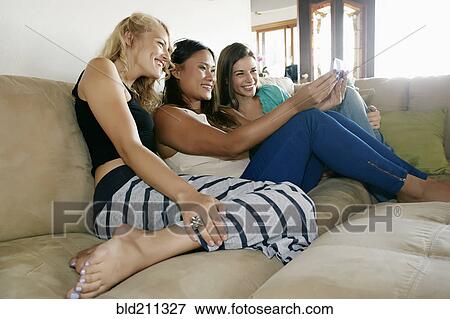 Stock Photo - Women taking self-portrait together on sofa. Fotosearch