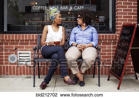 Stock Image - Women talking outside coffee shop on city street. Fotosearch