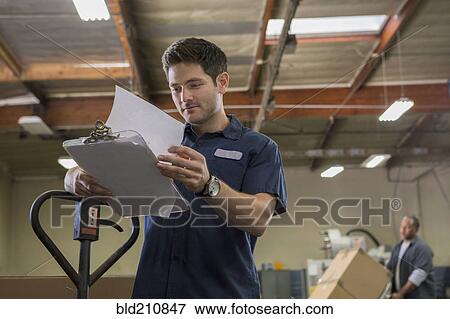 Stock Photo - Worker reading clipboard in warehouse. Fotosearch