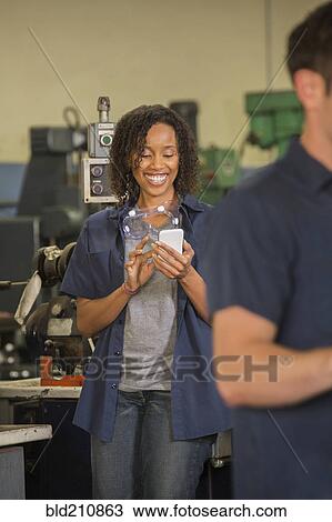 Stock Image - Worker using cell phone in warehouse. Fotosearch
