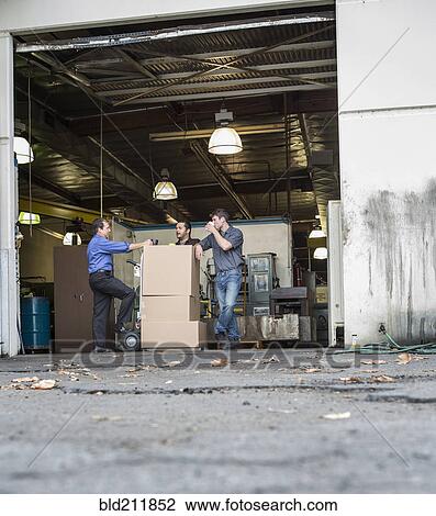 Stock Image - Workers enjoying coffee break at warehouse loading dock. Fotosearch