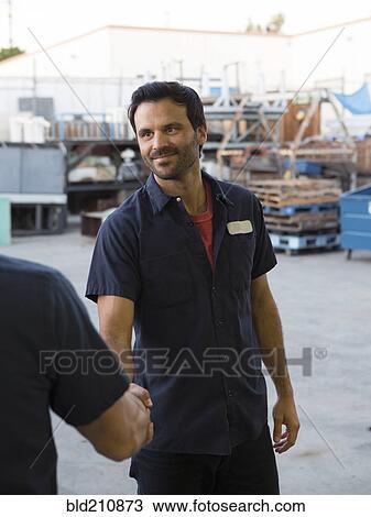Stock Image - Workers shaking hands in warehouse. Fotosearch
