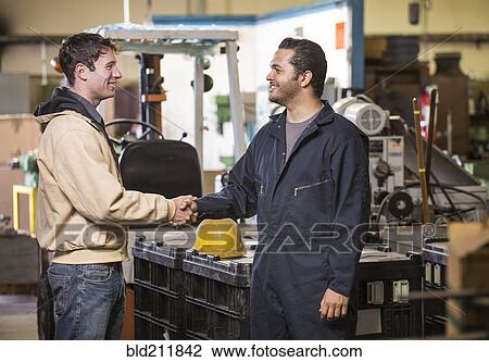 Stock Image - Workers shaking hands in warehouse. Fotosearch
