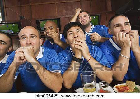 Stock Photo - Worried teammates watching television in sports bar. Fotosearch