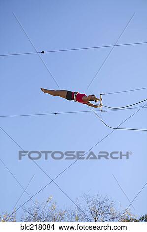 Acrobat hanging from trapeze under blue sky View Large Photo Image Picture - Acrobat hanging from trapeze under blue sky. Fotosearch