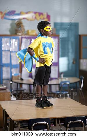 Stock Photo - African American boy in superhero costume standing on desk. Fotosearch