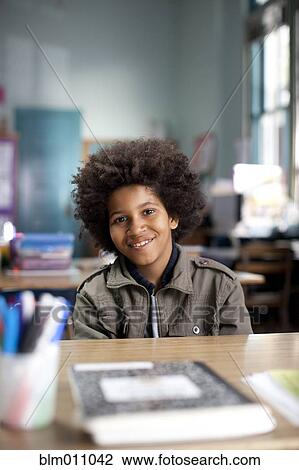Stock Image - African American boy sitting at desk in classroom. Fotosearch