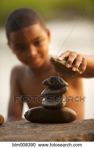 Stock Image - African American boy stacking rocks. Fotosearch