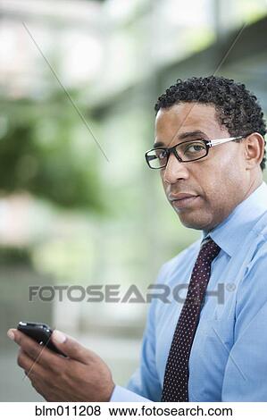 Stock Photo - African American businessman holding cell phone. Fotosearch
