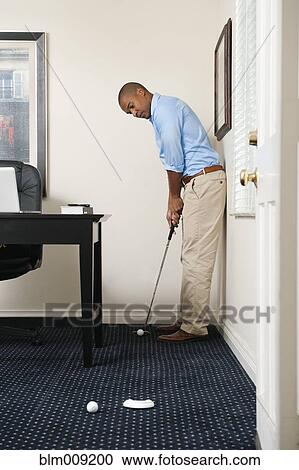 Stock Image - African American businessman putting golf ball. Fotosearch