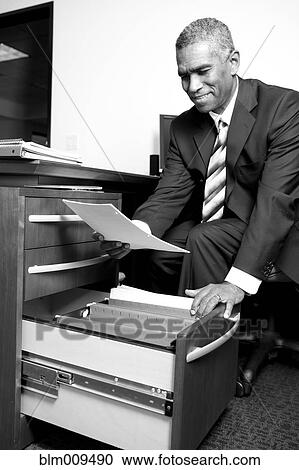 Stock Image - African American businessman putting paperwork in drawer. Fotosearch
