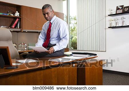 Stock Photograph - African American businessman sitting on desk. Fotosearch