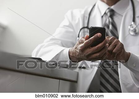Stock Image - African American doctor text messaging on cell phone. Fotosearch