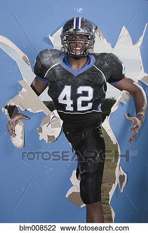 Stock Image - African American football player breaking through wall. Fotosearch
