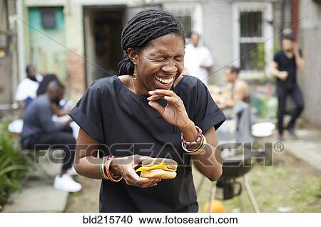 Stock Image - African American woman eating at backyard barbecue. Fotosearch