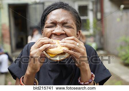 Stock Image - African American woman eating at backyard barbecue. Fotosearch