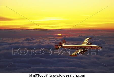 Airplane flying over clouds at sunset View Large Photo Image Stock Photo - Airplane flying over clouds at sunset. Fotosearch
