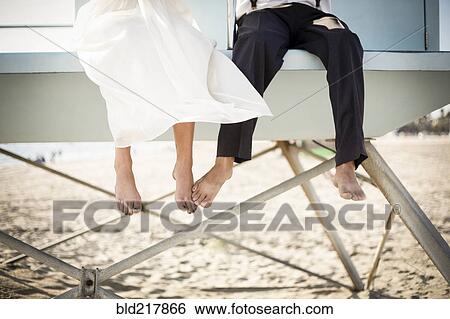 Stock Photograph - Asian bride and groom sitting on lifeguard hut on beach. Fotosearch