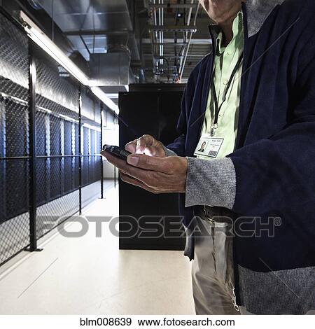 Stock Photo - Asian businessman using cell phone in office technology room. Fotosearch