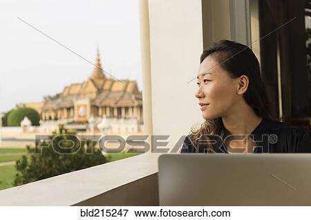 Stock Photo - Asian businesswoman admiring view from cafe window, Phnom Penh, Cambodia. Fotosearch