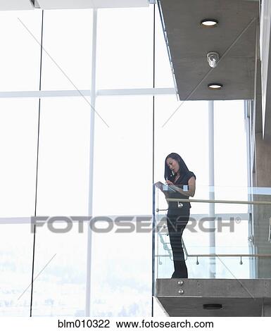 Stock Image - Asian businesswoman standing on internal office balcony. Fotosearch